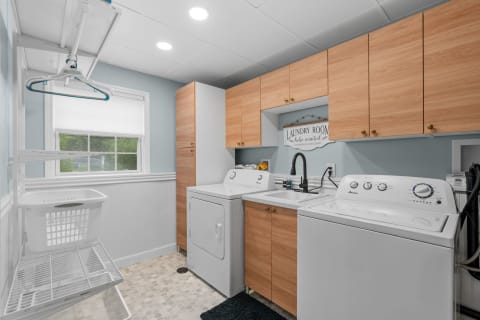 Modern laundry room with wooden cabinets, washing machine, and decorative sign.