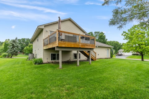 A residential house with a wooden deck in a green backyard.