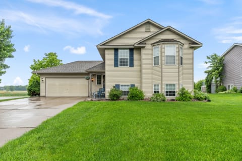 A suburban house with beige siding, blue shutters, and a well-kept lawn on a sunny day.