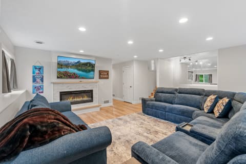 A spacious living room featuring blue sofas, a fireplace, and a mounted TV.