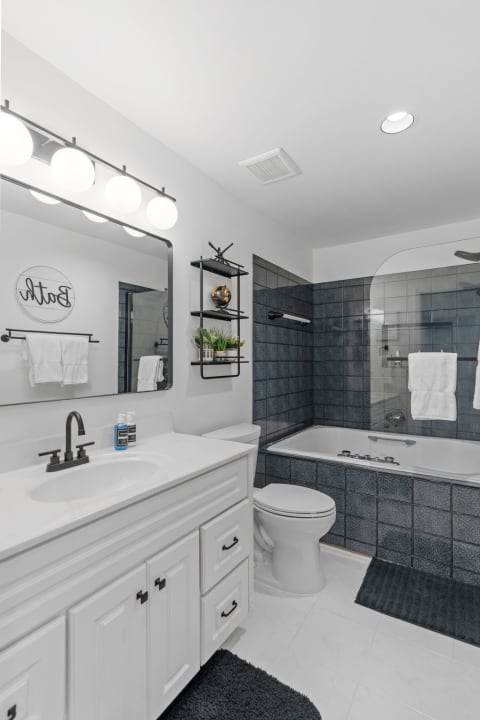 A stylish bathroom with a white vanity, large mirror, and blue tiled tub area, decorated with plants and white towels.