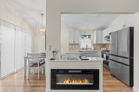 Modern kitchen and dining area with white cabinetry and electric fireplace.