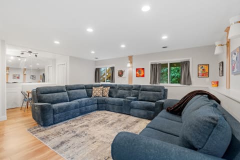 Spacious living room with a blue sectional sofa, artistic wall decor, and natural light from windows.