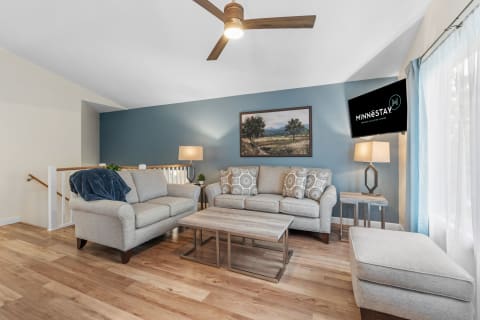 Cozy living room with light gray furniture, a landscape painting, and a mounted TV.