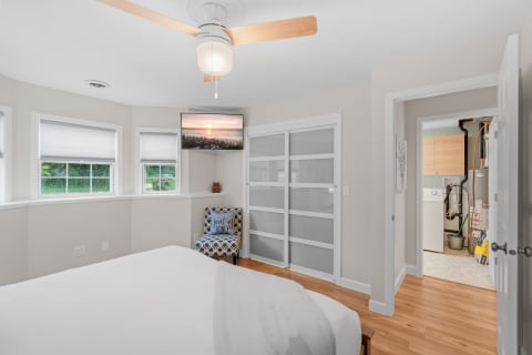 Cozy bedroom interior with a bed, a chair, windows, and a wall-mounted TV.