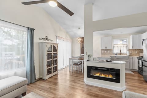 A contemporary living space featuring a white kitchen, dining area, and electric fireplace.