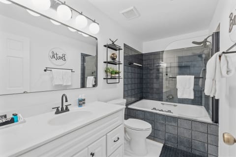 A contemporary bathroom featuring a white vanity, dark tiles, and decorative elements.