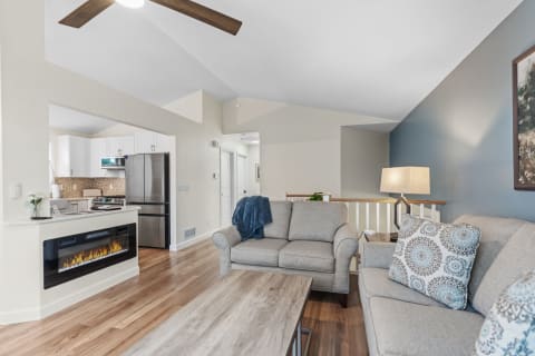 Modern living room with gray sofas, wooden coffee table, and a view of an open kitchen.