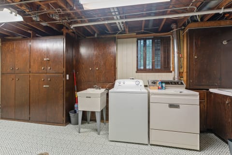 A functional basement laundry with dark cabinets, washing machine, and utility sink.