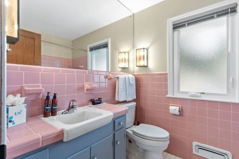 A bathroom featuring pink tiles, a blue vanity, and modern lighting.