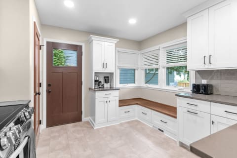 Modern kitchen featuring white cabinets, wooden countertop, and a cozy bench by the window.