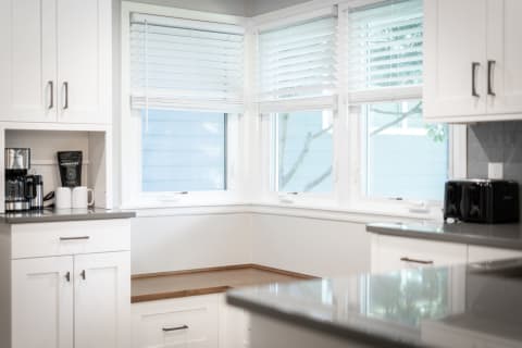 A modern kitchen corner featuring a coffee maker, two mugs, and a toaster by the window.