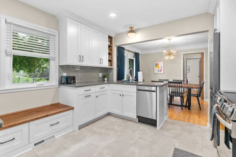 A modern kitchen with white cabinets, a wooden bench, and an adjacent dining area.