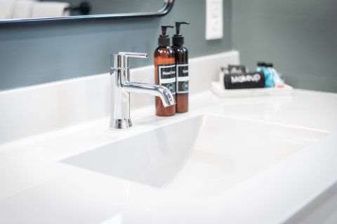A contemporary bathroom sink featuring a chrome faucet and amber glass bottles of hand sanitizer.