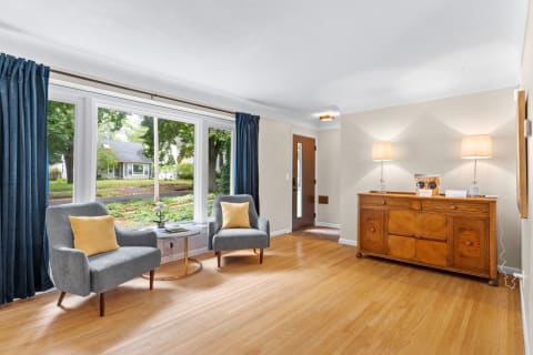 Cozy living room with grey chairs, yellow pillows, and a view of green trees outside.