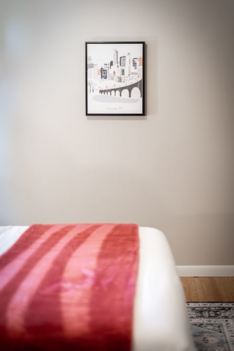 Cozy bedroom with a red striped blanket and a Minneapolis cityscape artwork on the wall.