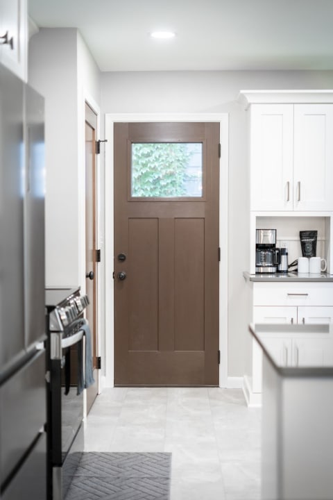 A view of a modern kitchen with a brown door and light gray walls.