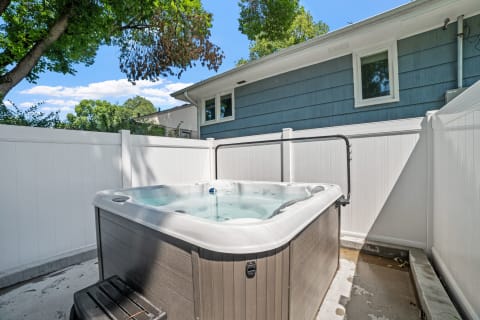 A hot tub in an outdoor area with a white fence and a blue house in the background.