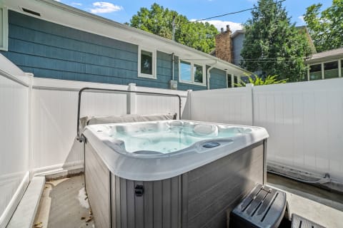 Hot tub in a backyard with a white fence and blue house in the background.