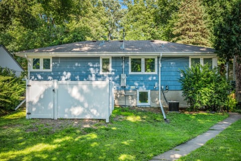 A split-level house with a blue exterior and a white fence on a sunny day.