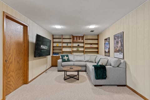Cozy basement living room with grey sectional sofa, movie posters, and wooden shelves.