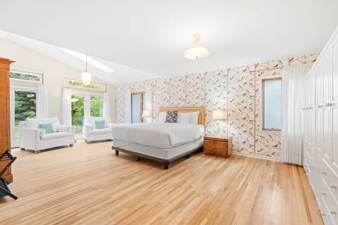 A bright bedroom featuring a large bed, white chairs, and floral wallpaper.