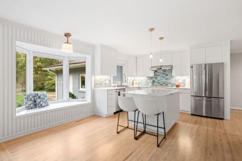 Modern kitchen featuring white cabinetry, a blue tile backsplash, and a cozy window seat.