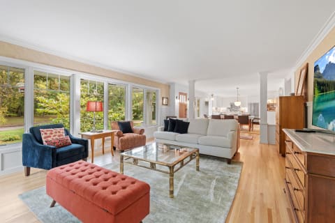 Spacious living room with large windows, cozy sofa, and colorful accent chairs.
