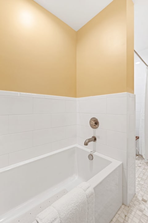 A modern bathroom with a white bathtub and yellow wall paint.