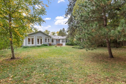 Backyard view of a single-story grey house with a patio and trees.