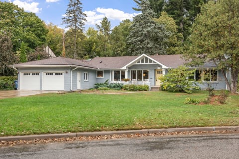 Single-story grey brick house with a brown roof and lush front lawn.