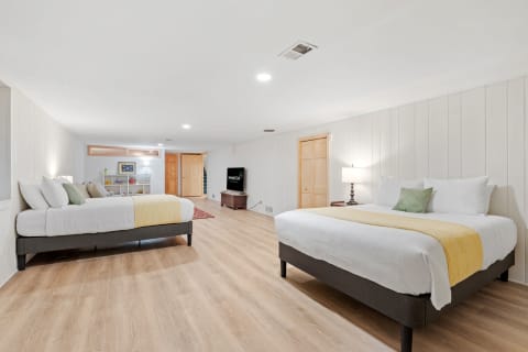 A modern bedroom featuring two beds, light wood flooring, and warm lighting.