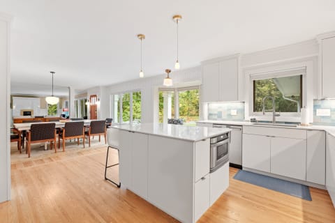 Bright and modern kitchen with a dining area, featuring white cabinets and a blue tile backsplash.