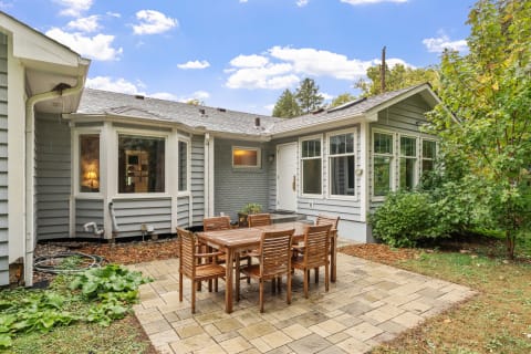 Outdoor dining space with a wooden table and gray house in the background.