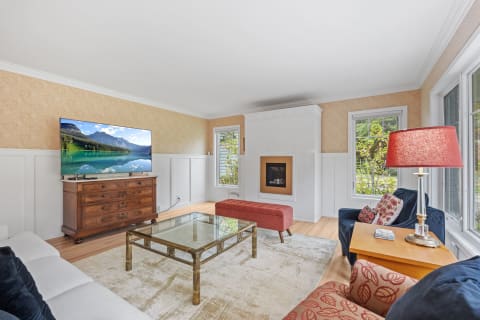 Bright living room with a TV, wooden dresser, fireplace, and colorful seating.