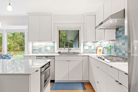 Contemporary kitchen with white cabinets, blue tile backsplash, and stainless steel appliances featuring natural light.