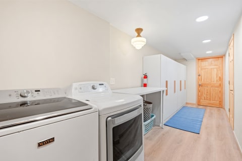 Laundry room featuring Maytag washer and dryer, white cabinetry, and wooden door.