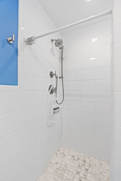 A bright shower space with white tiles, a chrome showerhead, and a blue-framed window.