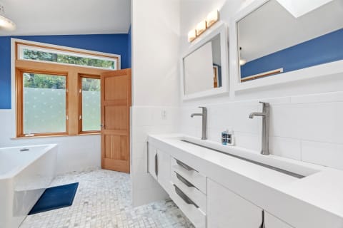 Modern bathroom featuring a blue wall, double vanity, and large windows.