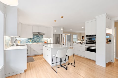 A contemporary kitchen with a white island, stools, and blue tile backsplash.