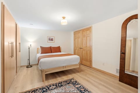 A well-lit bedroom featuring a queen-sized bed, wooden wardrobe, and decorative elements.