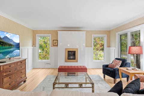 A cozy living room with a fireplace, large windows, and stylish furniture.