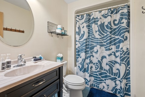 A bathroom with wave-pattern shower curtain, dark vanity, and decorative items on the counter.
