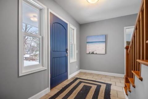 Entryway featuring a blue front door, beach artwork, and a striped rug.