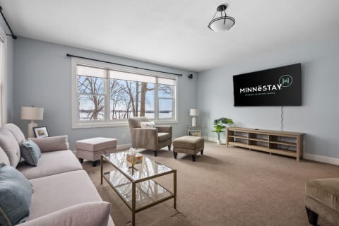 Modern living room with a couch, armchair, coffee table, TV, and a view of trees outside.