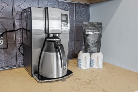 Modern coffee maker with a black coffee bag and two patterned mugs on a countertop.
