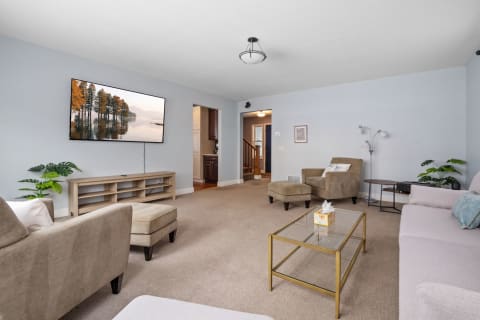 A modern living room featuring beige furniture, a large television showing a scenic nature view, and light blue walls.