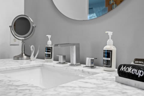 A contemporary bathroom sink with a marble countertop, chrome faucet, and skincare products.