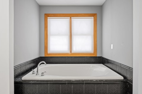 A modern bathroom featuring a white bathtub with black tiled walls and wood-framed windows.