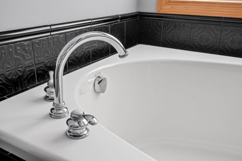 Close-up of a bathtub faucet with chrome fixtures and black tiled backsplash.